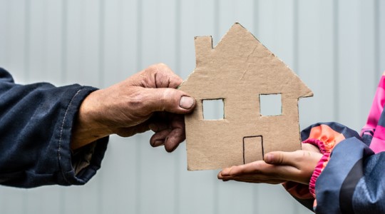 Hands holding a cardboard cutout of a house.